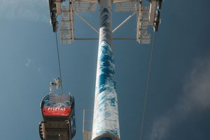 Widok od dołu na metalowy słup podpory kolei linowej Wildspitzbahn w Pitztal z grafika motywu górskiego oraz czerwoną gondolą po lewej stronie