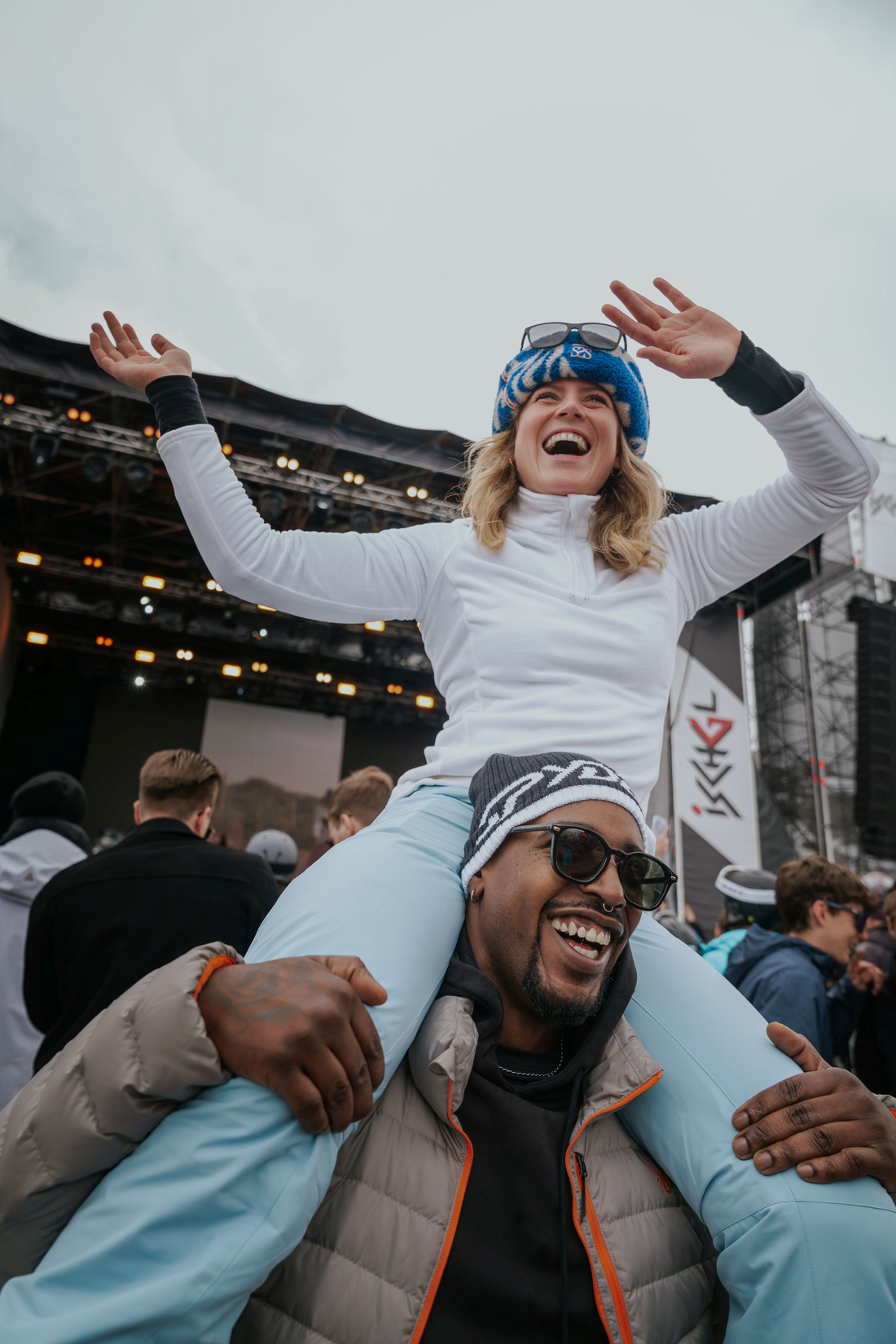 Radosna atmosfera i wspólna zabawa na koncercie Shaggy w Ischgl. Fot. © Flo Mitteregger Dwoje uśmiechniętych ludzi w zimowych czapkach i okularach przeciwsłonecznych przytula się podczas koncertu plenerowego w Ischgl.