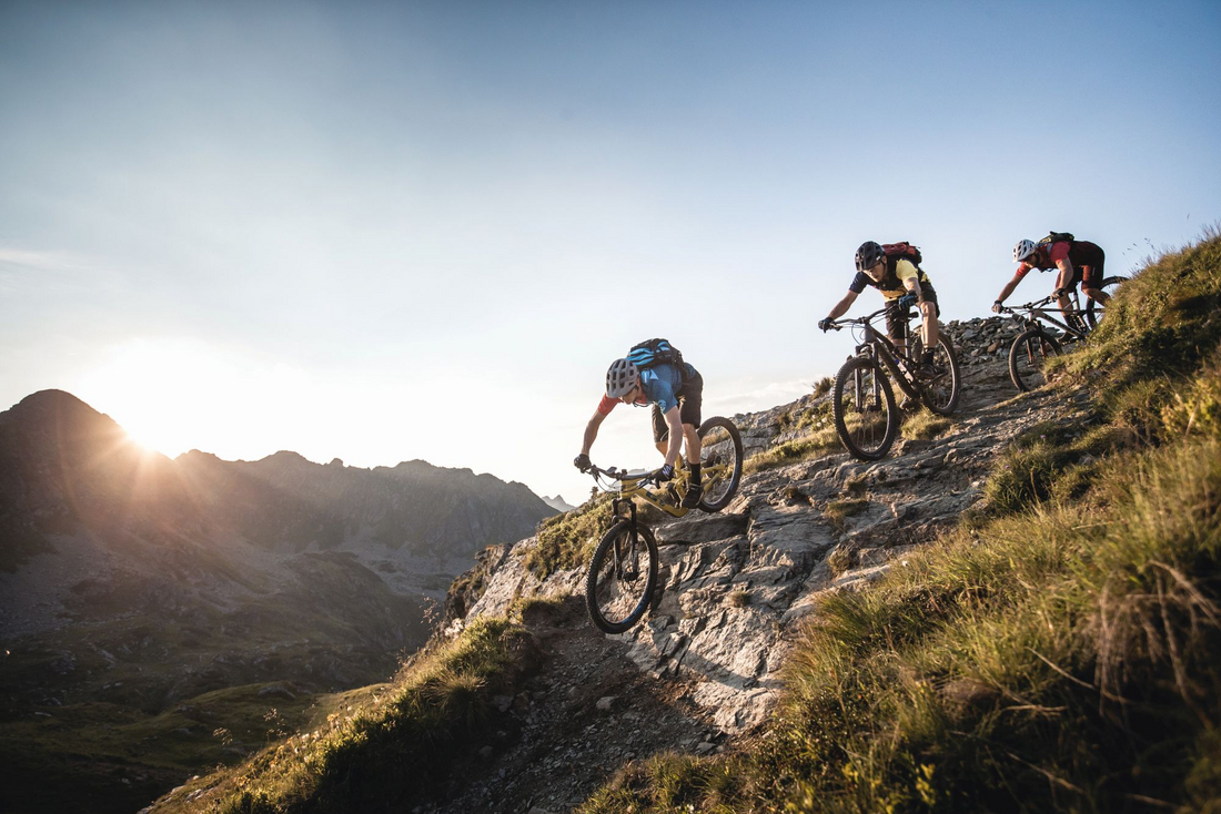 Trzech rowerzystów MTB na kamienistym technicznym zjeździe w Obertauern przy zachodzie słońca – trasy enduro w Alpach Salzburskich Trzech rowerzystów MTB na kamienistym technicznym zjeździe w Obertauern przy zachodzie słońca – trasy enduro w Alpach Salzburskich