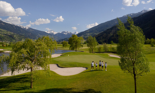 Grupa osób w białych koszulkach i ciemnych spodenkach na polu golfowym w górach