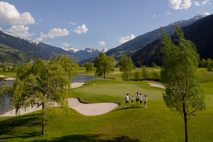 Grupa osób w białych koszulkach i ciemnych spodenkach na polu golfowym w górach