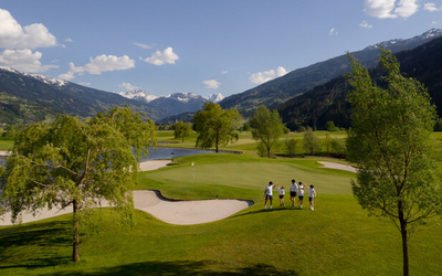 Grupa osób w białych koszulkach i ciemnych spodenkach na polu golfowym w górach