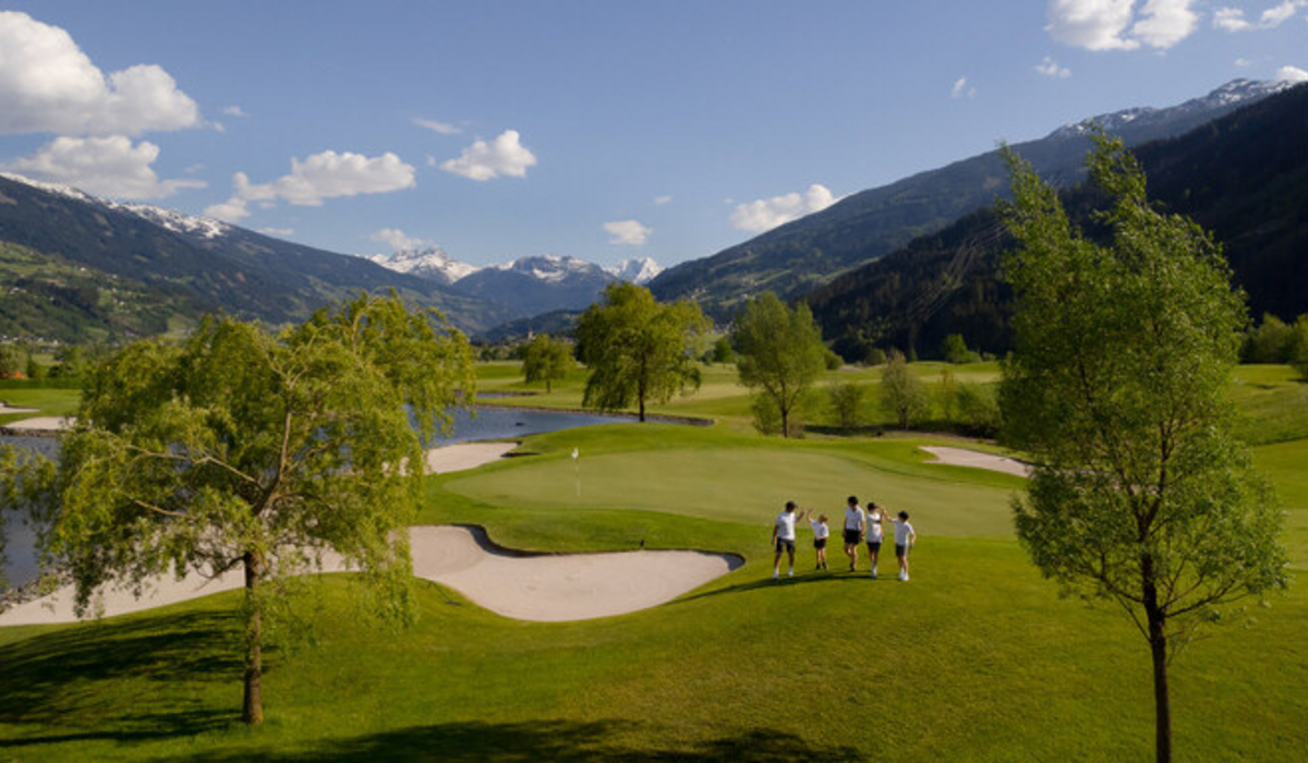 Pole golfowe w Tyrolu © Zillertal Tourismus / Phillip Geisler Grupa osób w białych koszulkach i ciemnych spodenkach na polu golfowym w górach