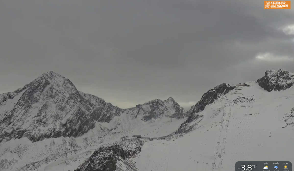 Widok z kamery internetowej - Stubai 23 10 2026 / https://www.stubai.at/pl/kamery-live/? Zaśnieżone szczyty nad lodowcem Stubai przy pochmurnym niebie