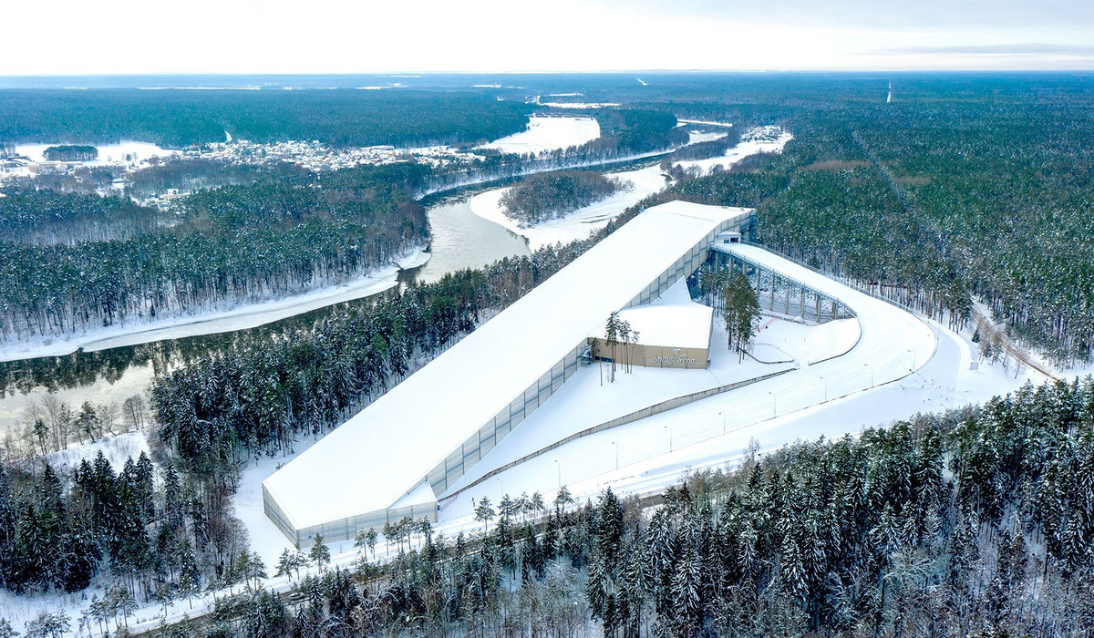 Całoroczna hala narciarska z lotu ptaka – Architektura Snow Arena Druskienniki Widok z lotu ptaka na Hale Narciarską z zewnętrzną trasą kompleks narciarski w otoczeniu zaśnieżonego lasu i zakola rzeki