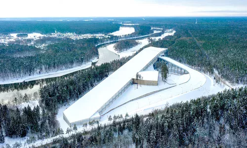 Całoroczna hala narciarska z lotu ptaka – Architektura Snow Arena Druskienniki Widok z lotu ptaka na Hale Narciarską z zewnętrzną trasą kompleks narciarski w otoczeniu zaśnieżonego lasu i zakola rzeki
