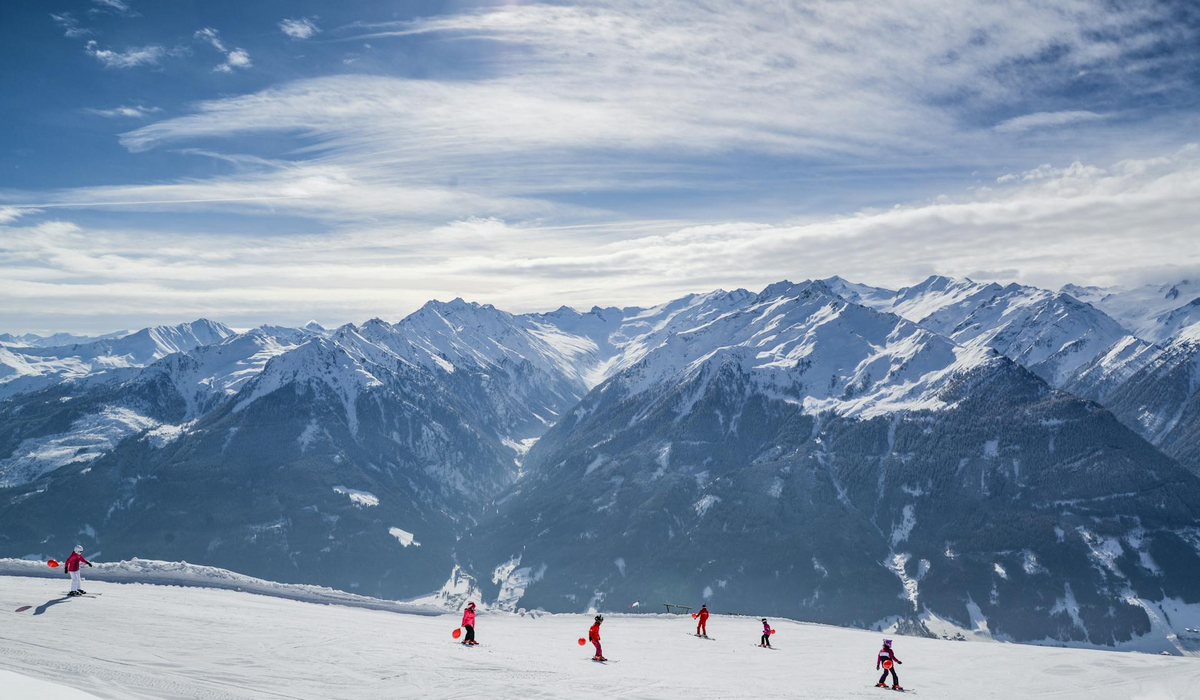 6 osób jeździ na nartach, w tle góry